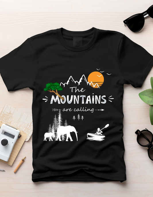 Mountains - DoodleChic 100% Organic Cotton Black Printed Kids T-shirt laid flat on desk with camera and plant, showcasing outdoor-themed print.