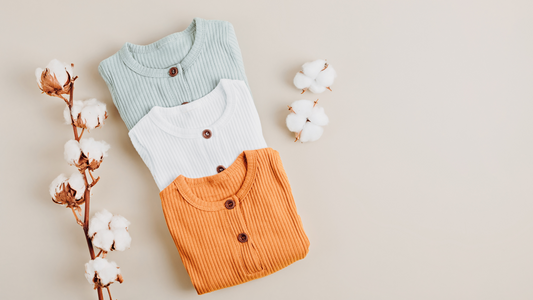 Stack of kids' organic cotton shirts in pastel colors with cotton branches.
