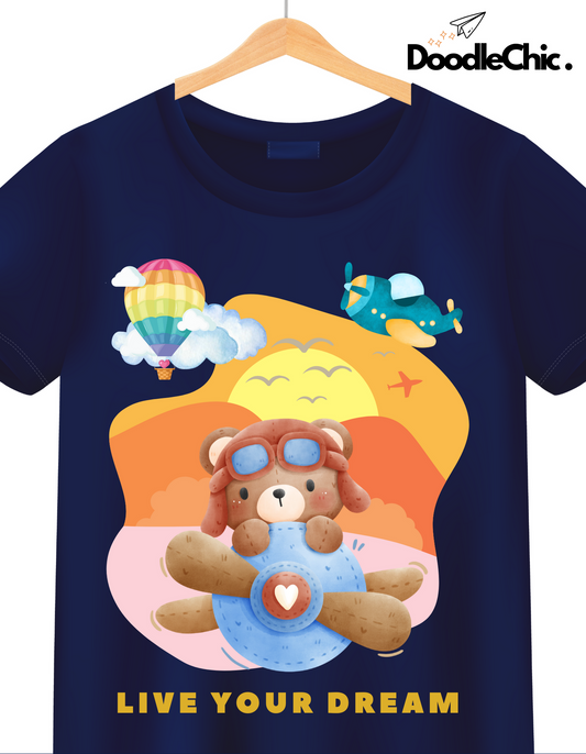 Close-up of Live Your Dream - DoodleChic Organic Cotton Navy Blue Kids T-shirt with colorful sky scene and adventurous teddy bear pilot graphic.