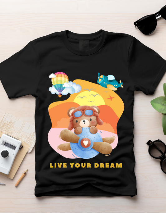 Live Your Dream by DoodleChic - 100% Organic Cotton Black Kids T-shirt laid flat on a desk, showcasing playful bear pilot design and vibrant colors.