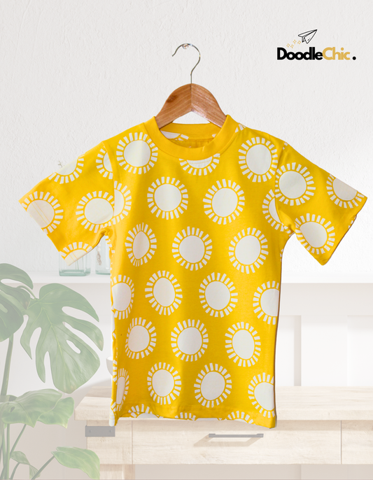 Morning Sunshine by DoodleChic - 100% Organic Cotton Kids T-shirt with sun print, hanging in a cozy home setting with natural decor for conscious kidswear.