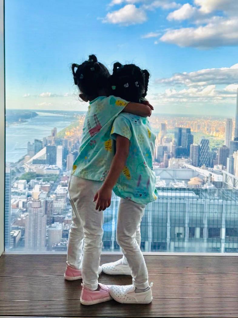 Two children hugging with a cityscape view in the background. Bunny Hop Delight 100% Organic Cotton Girls Top from DoodleChic