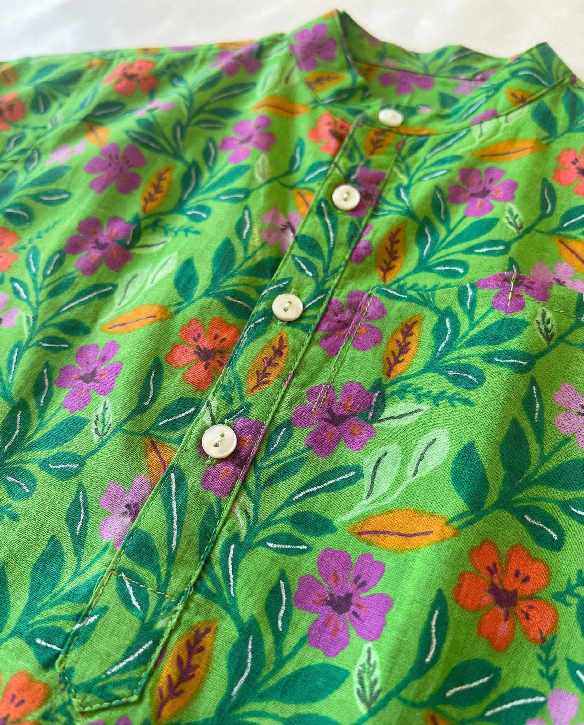 Green floral shirt with colorful flowers and leaves on a white background