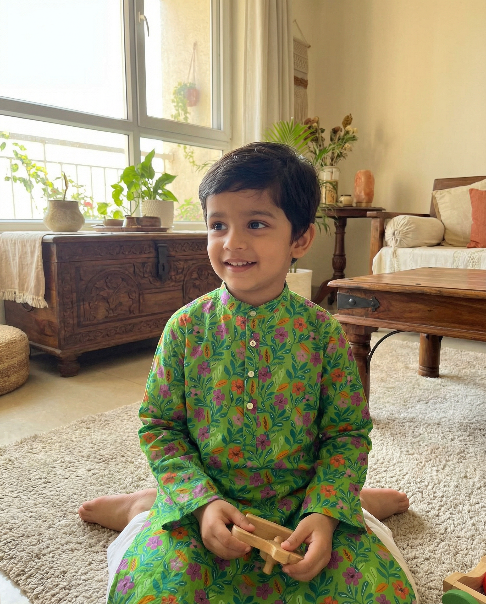 Child in a green floral outfit sitting on the floor in a living room.
