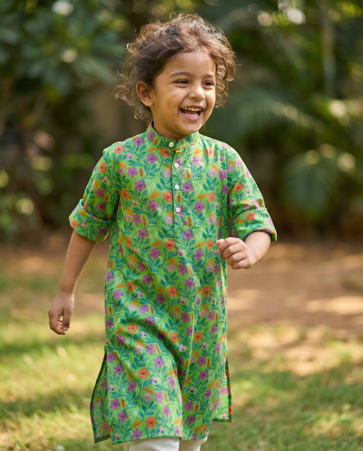 Child wearing a green floral kurta standing outdoors with a blurred natural background